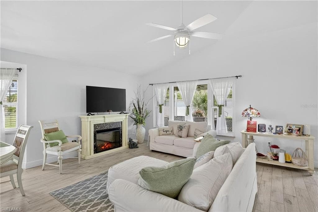 Spacious living area featuring light wood-finish flooring, an electric fireplace with a decorative mantel, and a vaulted ceiling with a ceiling fan