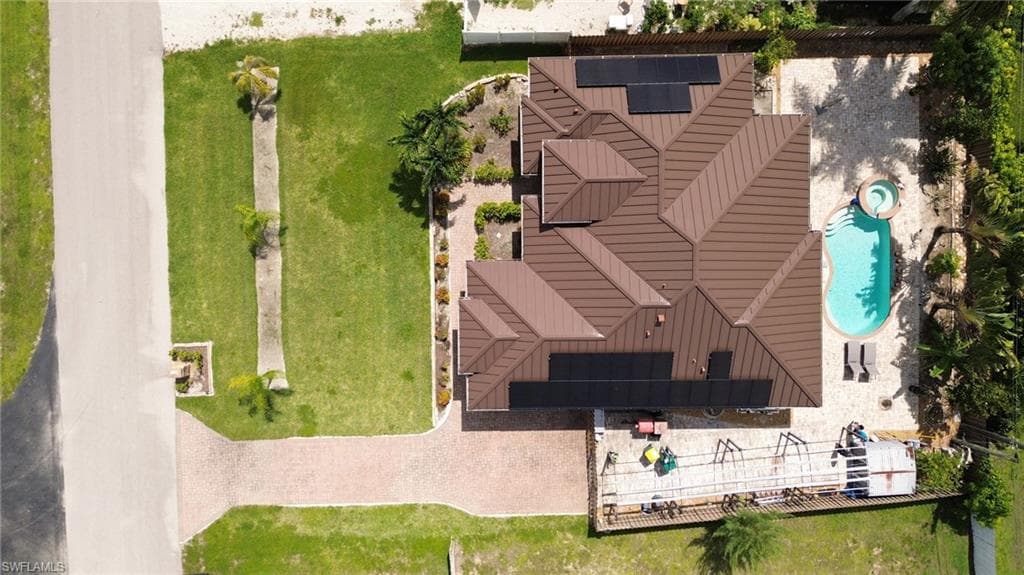 Expansive property featuring a brown metal roof, solar panels, a swimming pool with an integrated spa, and a paver driveway