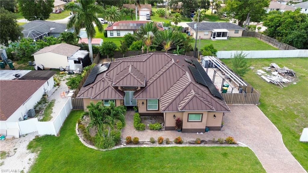 Contemporary residence featuring a brown tile roof with integrated solar panels, a paver driveway, manicured front lawn, mature landscaping, and an enclosed side patio