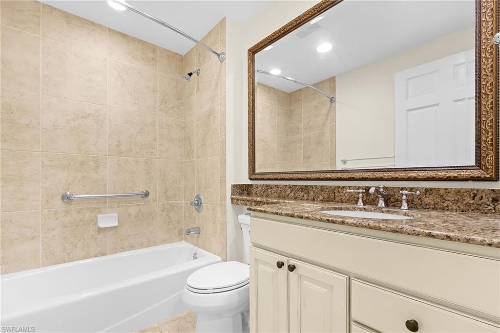 Bathroom featuring a spacious tub, tiled shower surround, and a vanity with a stone-finish countertop