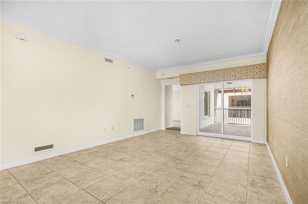Spacious room featuring neutral-toned tile flooring, crown molding, and a full-wall sliding glass door opening to a private outdoor space