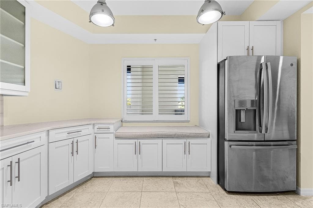 Kitchen area featuring a built-in window seat, white cabinetry with contemporary hardware, light-toned countertop, stainless steel refrigerator, and tiled flooring