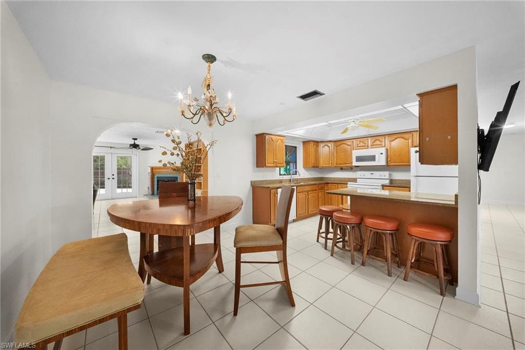 Kitchen featuring wood cabinetry, white appliances, a breakfast bar with seating, light-colored tile flooring, and a recessed ceiling fan