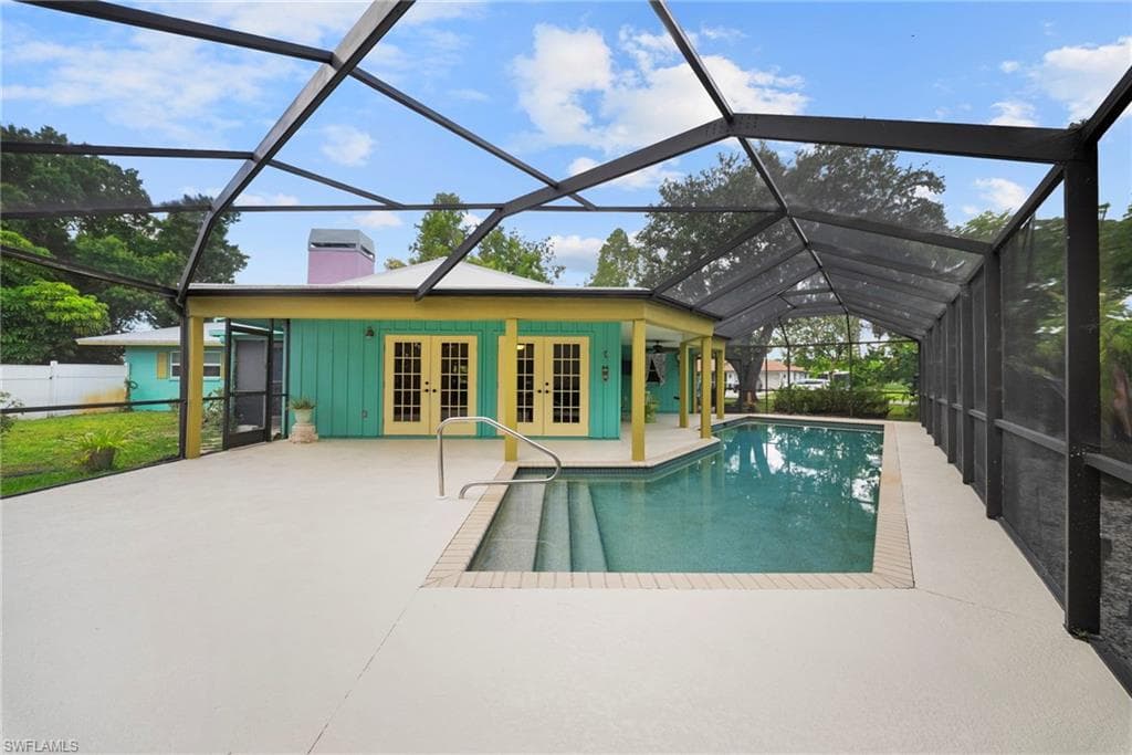 Screen-enclosed pool area featuring an in-ground swimming pool with steps, a spacious light-colored patio, and a structure with double French doors and a screened entry