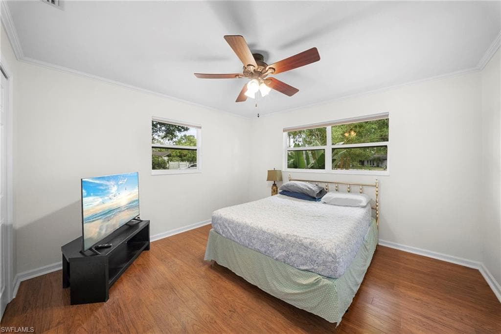 Bedroom featuring wood-finish flooring, two windows, crown molding, and a ceiling fan with integrated lighting
