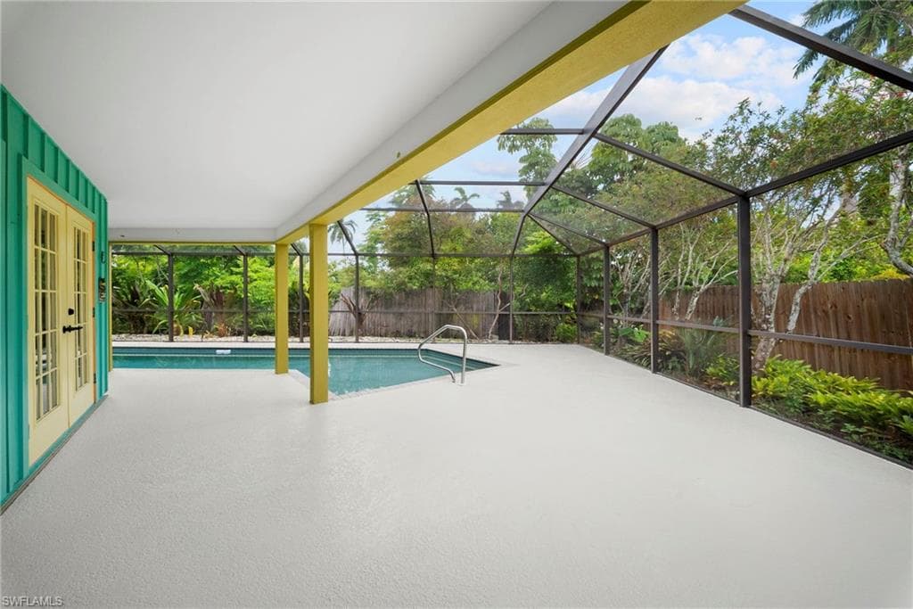 Screened pool enclosure with a light-colored paved deck, surrounded by lush tropical landscaping and a wooden fence