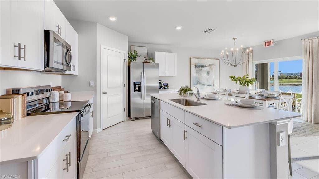 Model home. Kitchen with stainless steel appliances, suspended lighting, white cabinetry, and a center island with sink