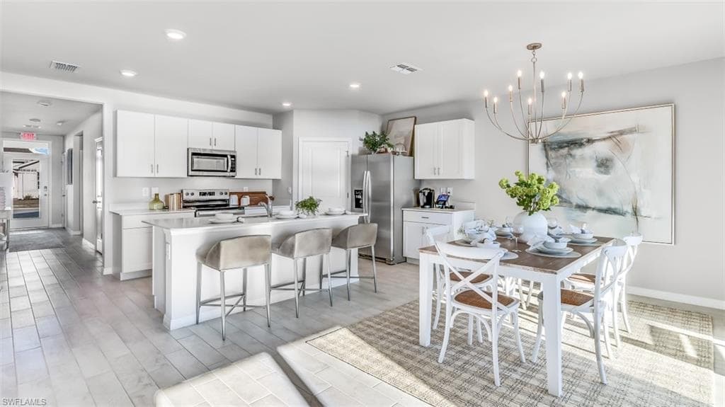 Model home. Kitchen with light countertops, white cabinetry, stainless steel appliances, an island with sink, and a breakfast bar