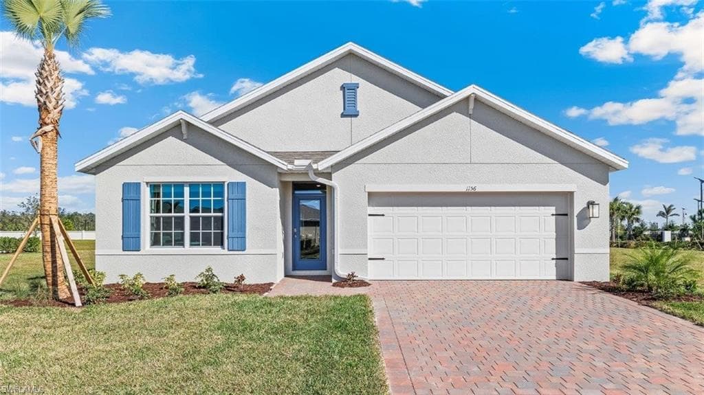 Model home. View of front of home with a front lawn, decorative driveway, a garage, and stucco siding