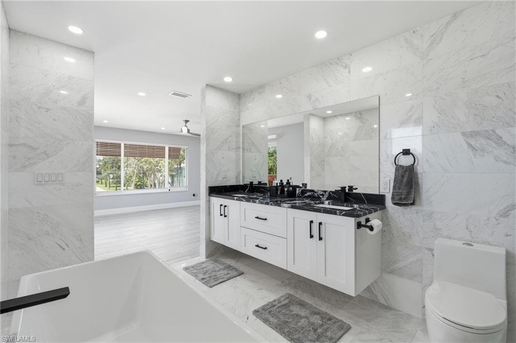 Contemporary bathroom featuring a floating dual vanity with black countertops, a deep soaking tub with a matte black faucet, and a wall-mounted toilet
