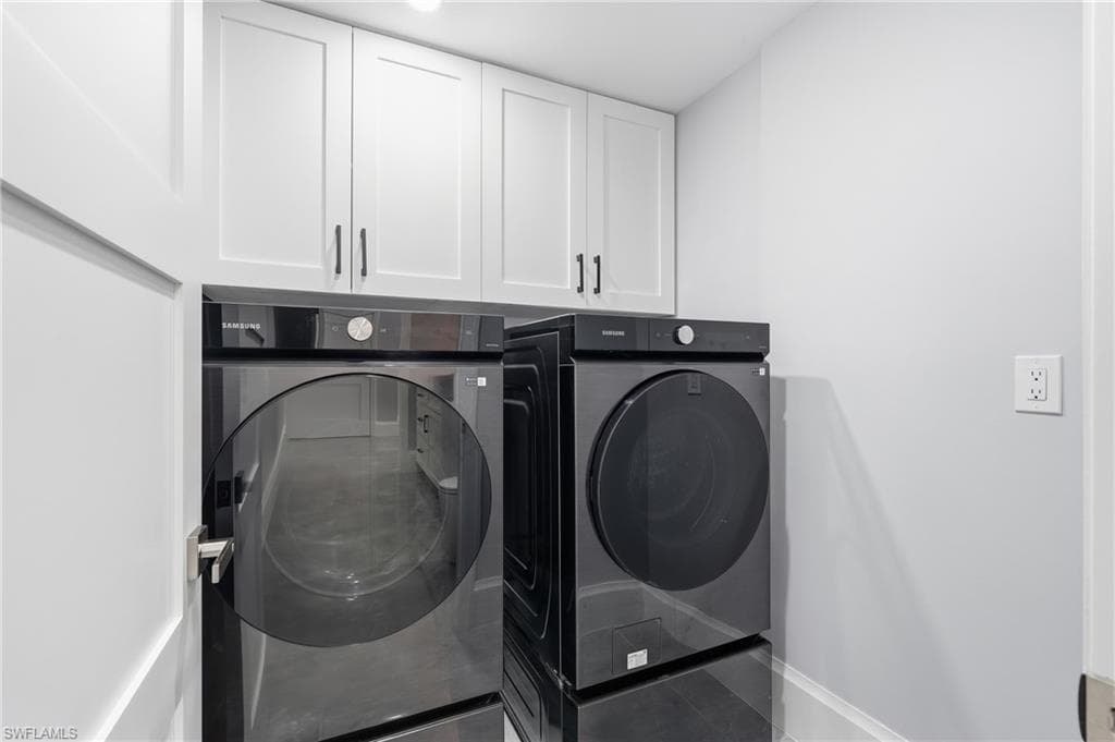 Laundry area featuring white shaker-style cabinetry with matte black hardware, light gray wall paint, and a white baseboard trim