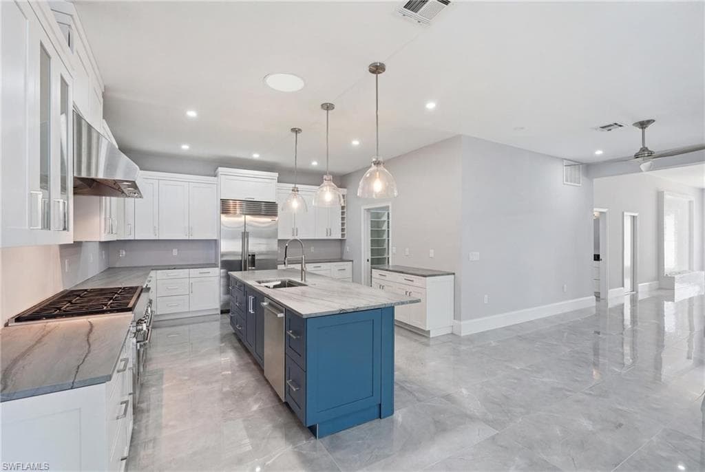 Modern kitchen featuring a blue island with sink, white perimeter cabinetry, stainless steel appliances, and light-toned countertops