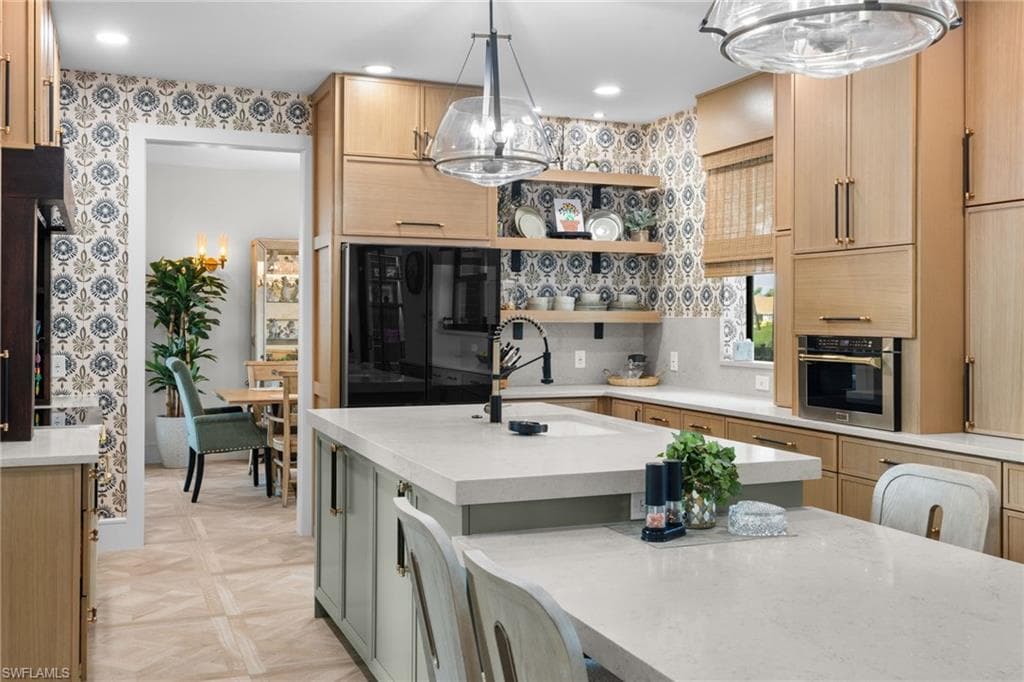 Gourmet kitchen featuring a central island with integrated seating, light wood-finish cabinetry, built-in stainless steel appliances, and decorative accent wallpaper