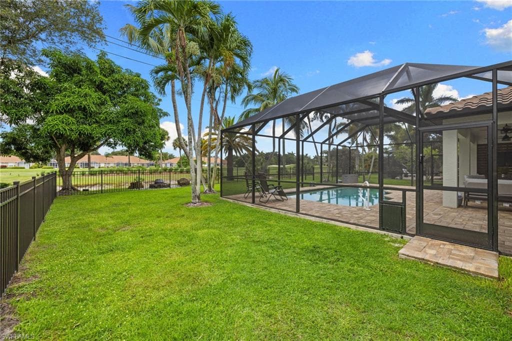 Expansive backyard featuring a screened-in pool enclosure, swimming pool, paver deck, and black metal fencing