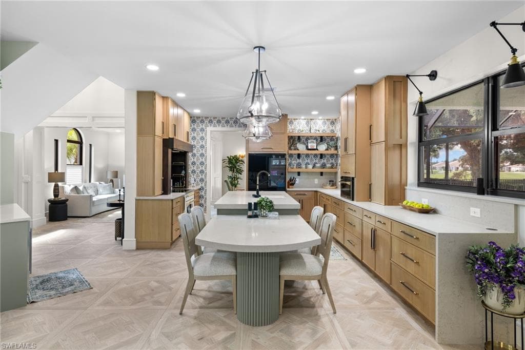 Open-concept kitchen featuring extensive light wood cabinetry, stone countertops, integrated appliances, and a central island with an undermount sink