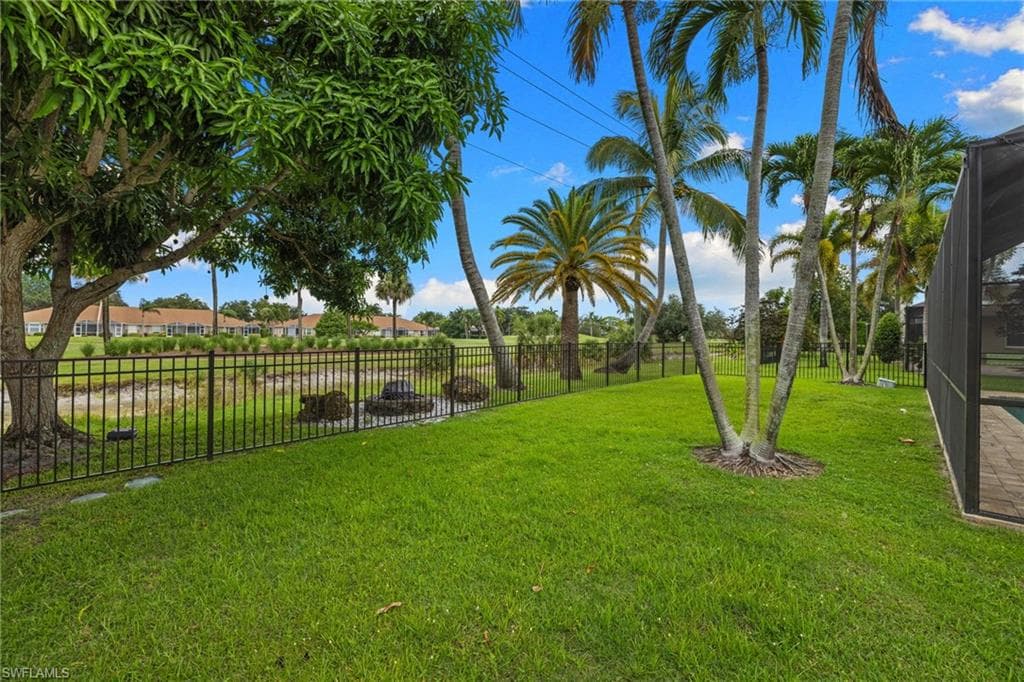 Expansive backyard featuring a lush lawn, mature palm trees, and a black wrought iron fence bordering a water feature