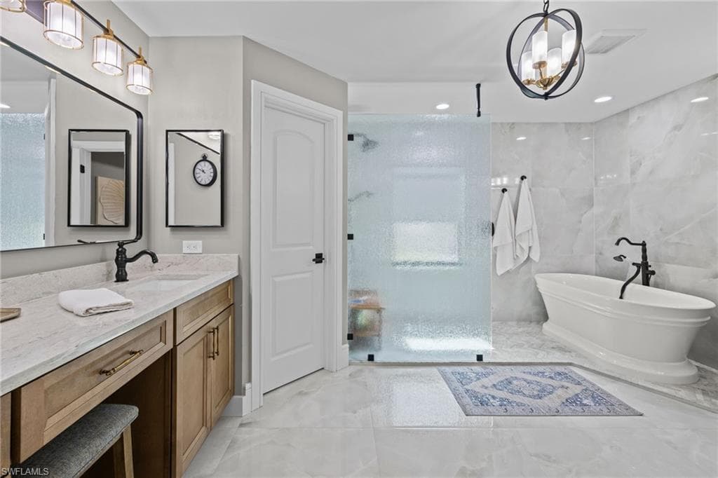 Well-appointed bathroom featuring a freestanding soaking tub, a frameless frosted glass shower enclosure, a double vanity with stone countertops, and large format wall and floor tiling