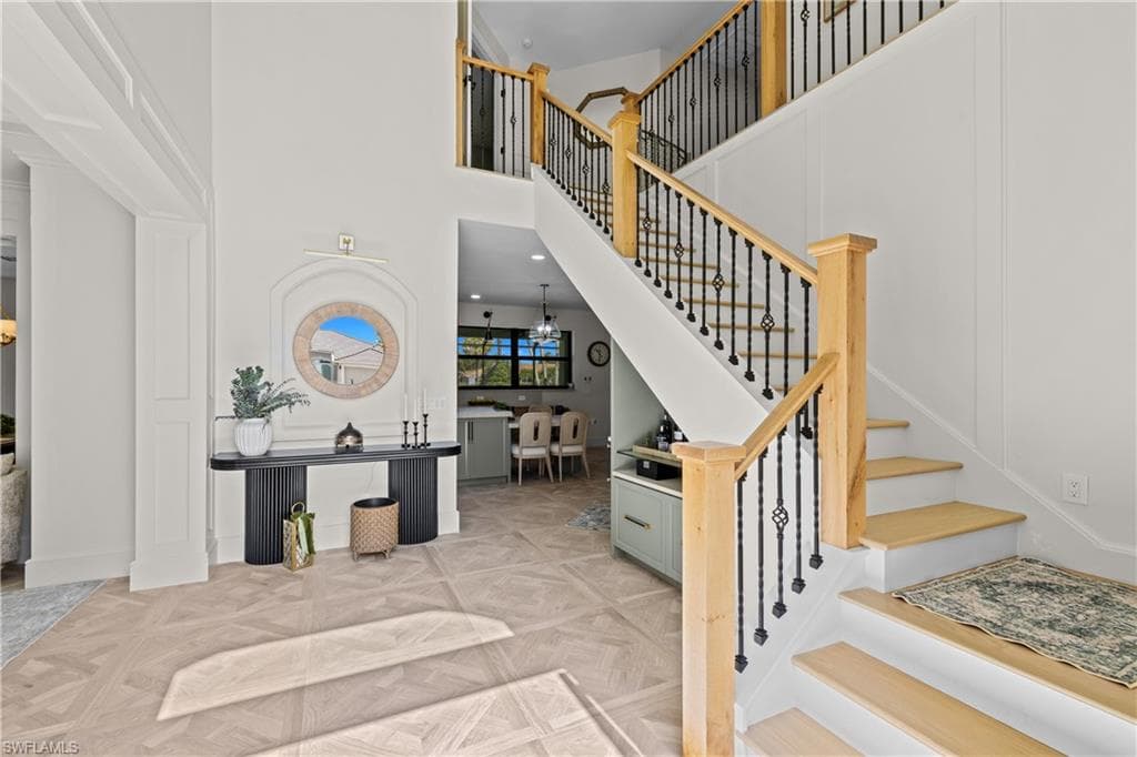 Grand entry foyer featuring a light wood staircase with wrought iron balusters and wood-finish flooring