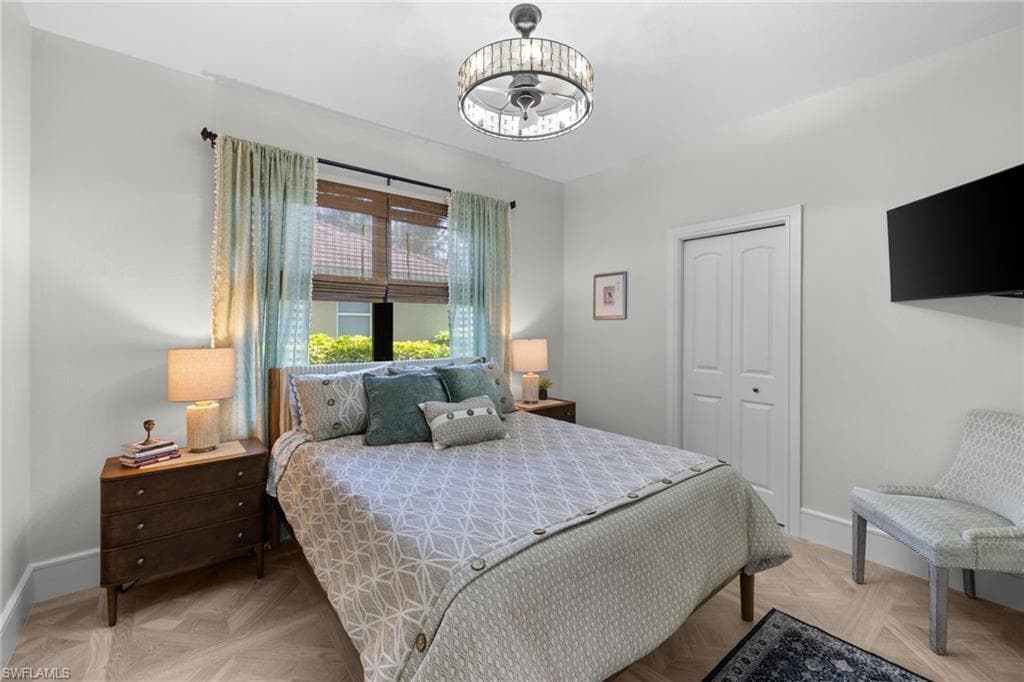 Bedroom featuring wood-finish herringbone flooring, a crystal-banded ceiling fan with integrated lighting, and a window with both woven wood shades and drapery
