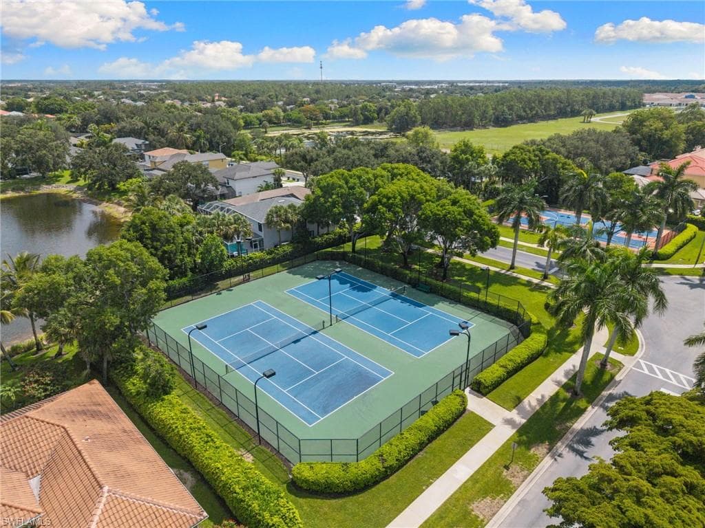 Two fenced tennis courts with light blue playing surfaces and green surrounds