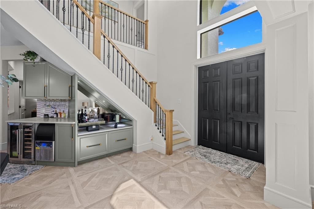 Foyer featuring a grand staircase with wrought iron balusters and natural wood handrails, a built-in wet bar with cabinetry and integrated wine refrigerators, light wood-finish parquet flooring, and a double-door entry with an arched transom window