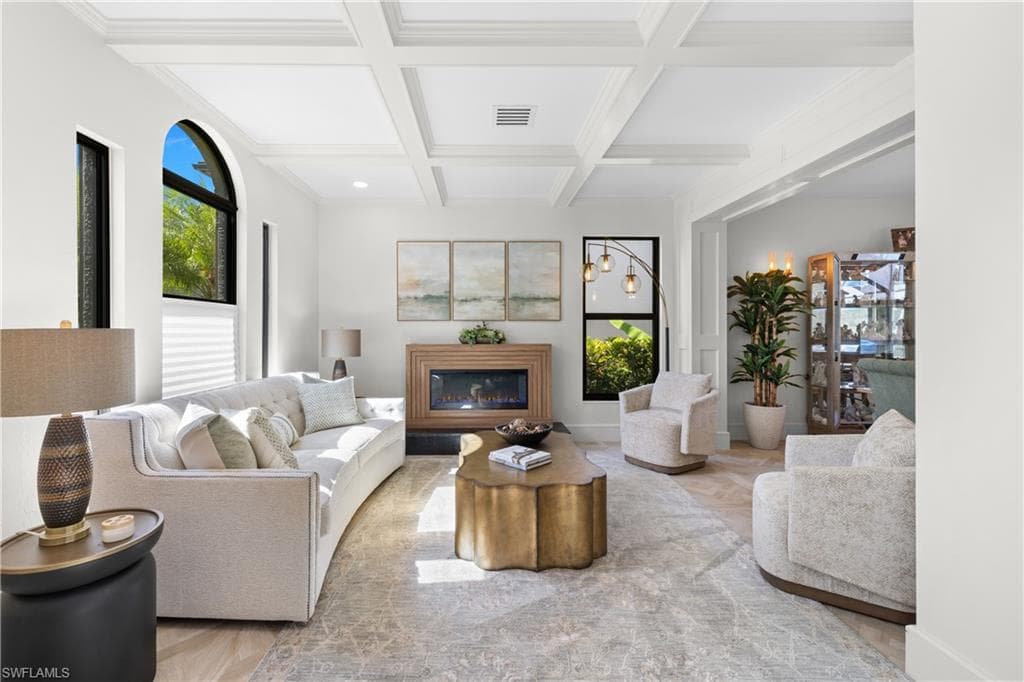 Living area featuring coffered ceilings, light-toned tile flooring, and an integrated fireplace with a wood-finish mantel