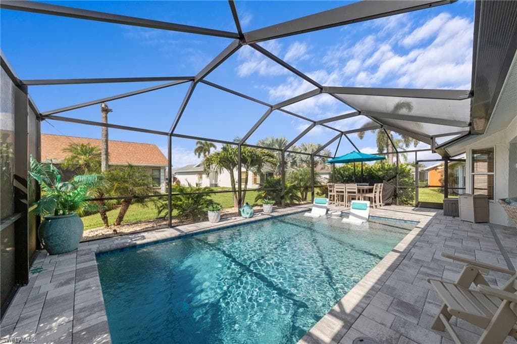 Screened-in outdoor living space featuring a heated saltwater pool with an integrated sun shelf, paver decking, and a covered patio area