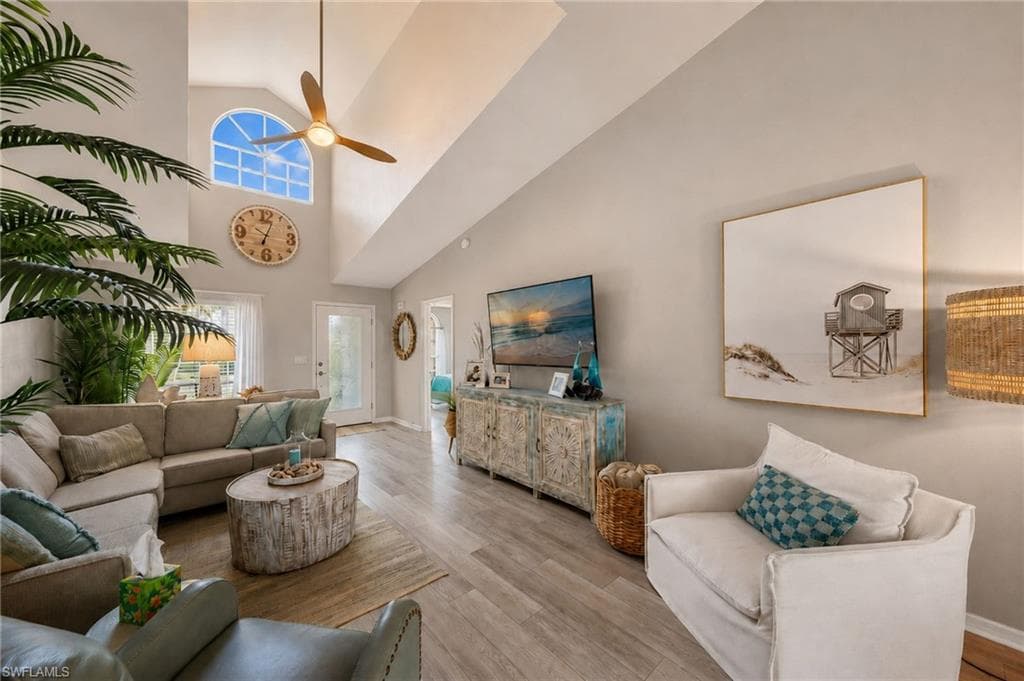 Vaulted ceiling living area featuring a large arched window, wood-finish flooring, a ceiling fan, and recessed lighting