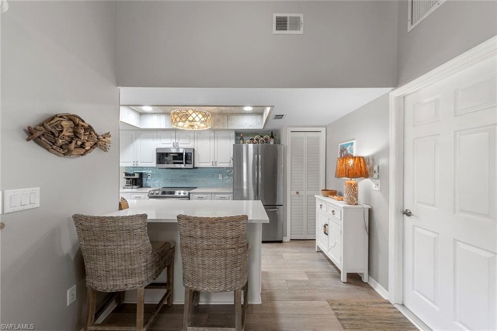 Open kitchen featuring a breakfast bar with seating, stainless steel appliances, white cabinetry, and a light blue tile backsplash