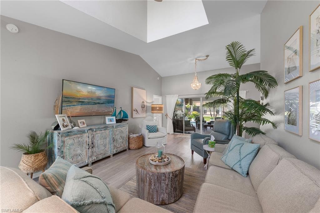 Spacious living area featuring light-toned wood-finish flooring, vaulted ceilings with skylight, and sliding glass doors providing access to an outdoor patio