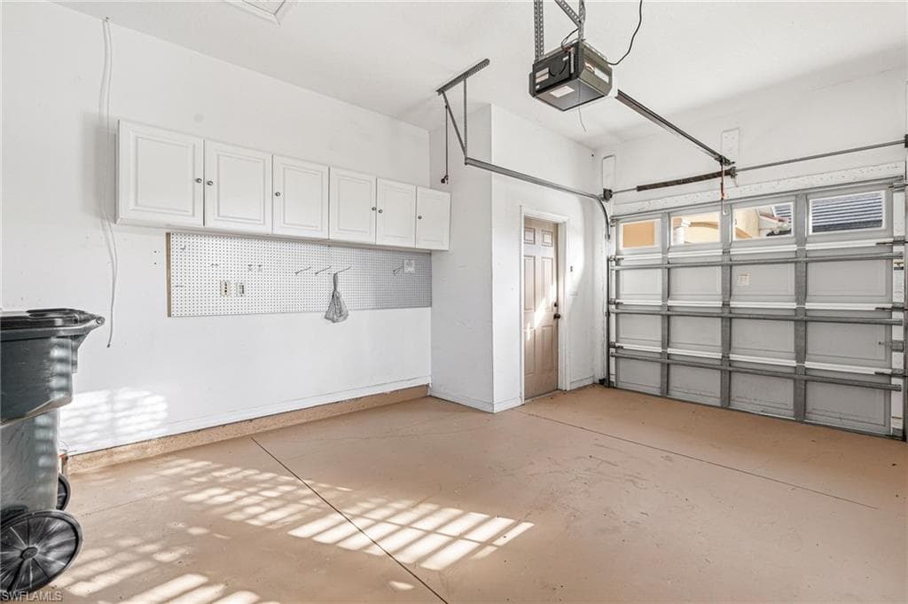 Garage space featuring an automatic overhead door, overhead storage cabinetry, pegboard organization, an interior access door, and a finished concrete floor