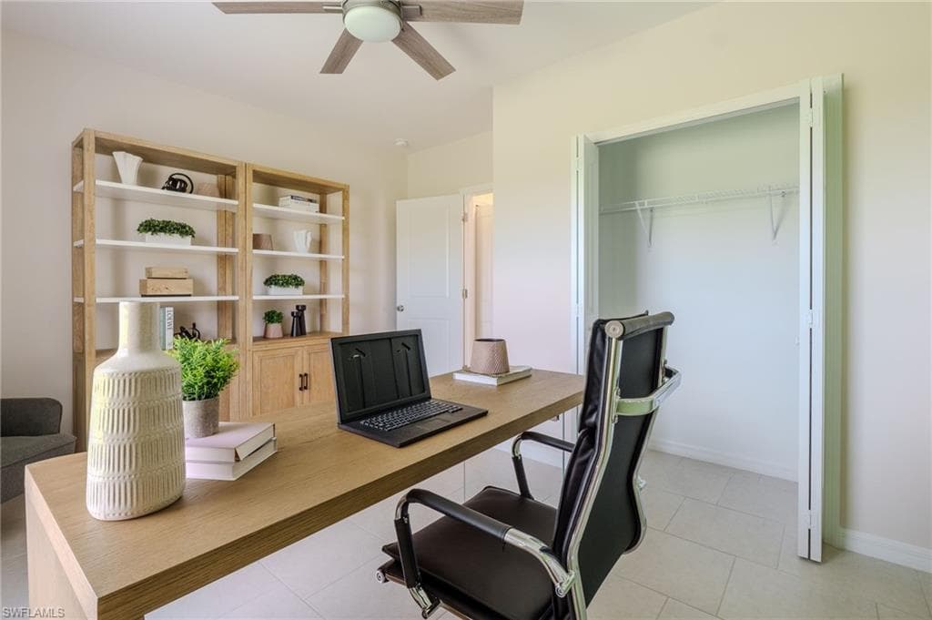 Dedicated office space featuring light-toned flooring, built-in shelving with lower cabinetry, a ceiling fan with integrated lighting, and a bi-fold closet with wire shelving