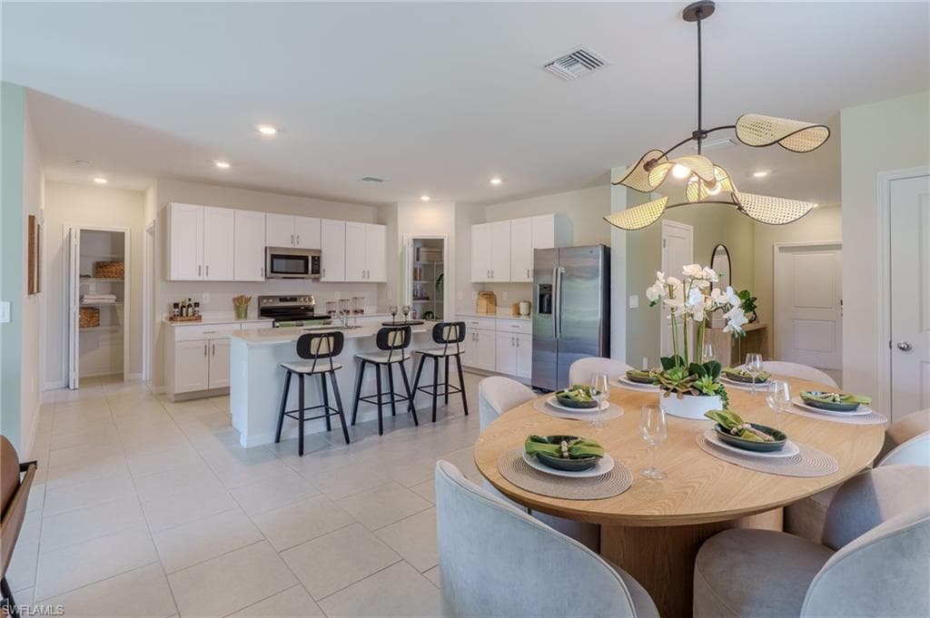 Open-concept kitchen and dining area featuring a kitchen island with seating, stainless steel appliances, white cabinetry, and recessed lighting
