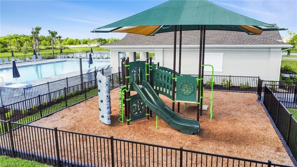 Fenced playground area featuring a play structure with a slide, a climbing wall, and a shade canopy
