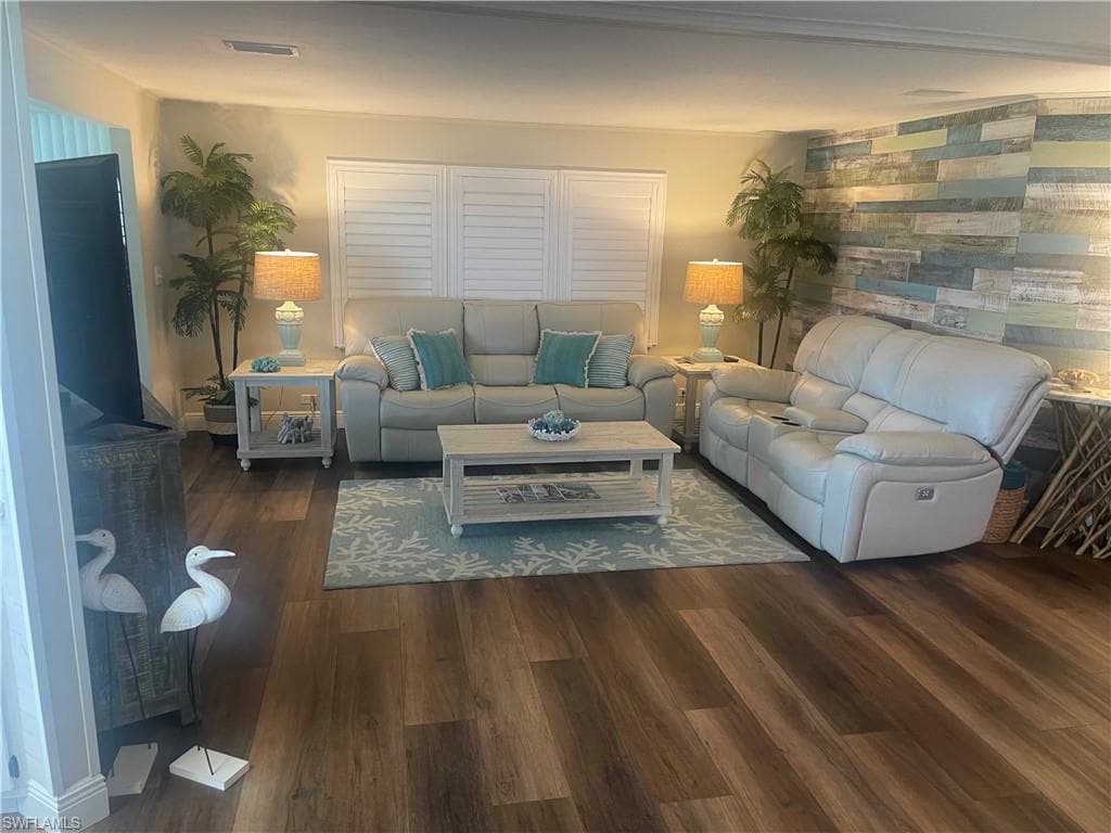Spacious living area featuring wood-finish flooring, white plantation shutters, and a multi-tone wood plank accent wall