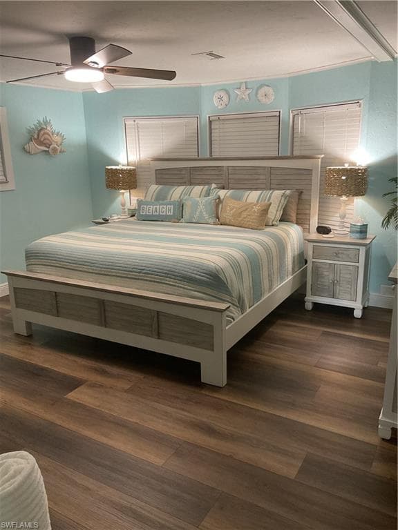Spacious bedroom featuring wood-finish flooring, a ceiling fan with integrated lighting, and multiple windows with blinds