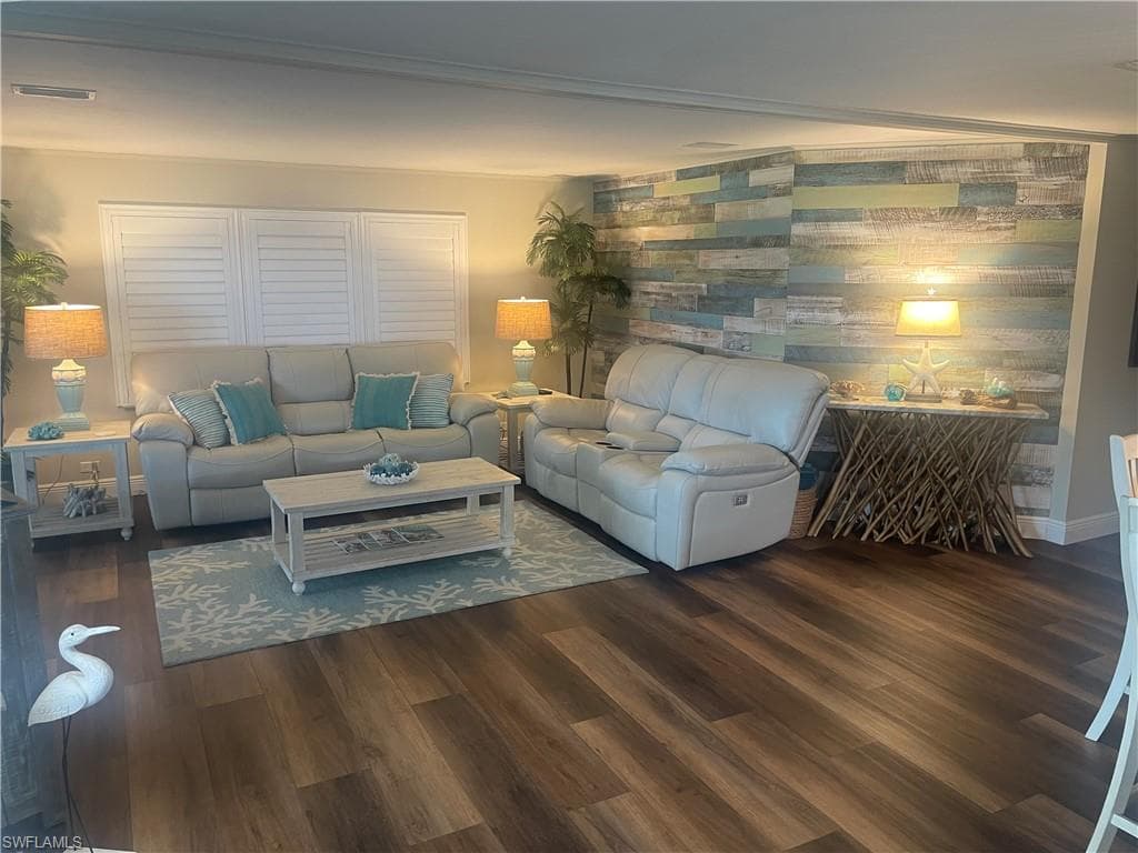 Living area featuring wood-finish flooring, a decorative accent wall with varied wood paneling, and a window with white plantation shutters