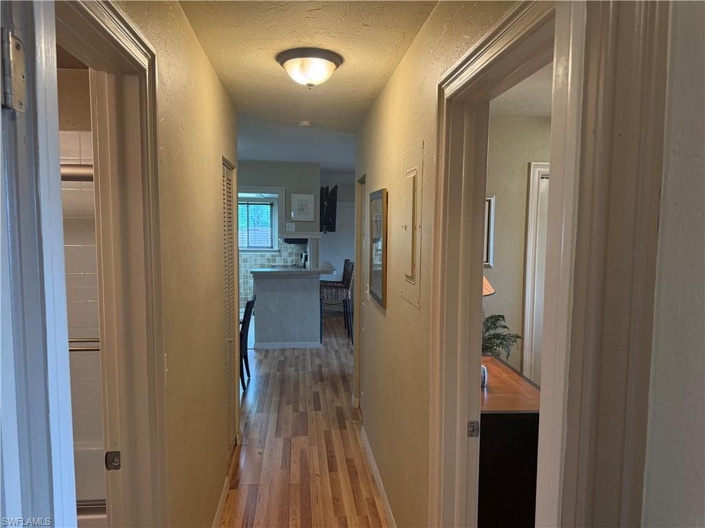 Hallway featuring wood-finish flooring, a flush-mount ceiling light, and access to additional rooms