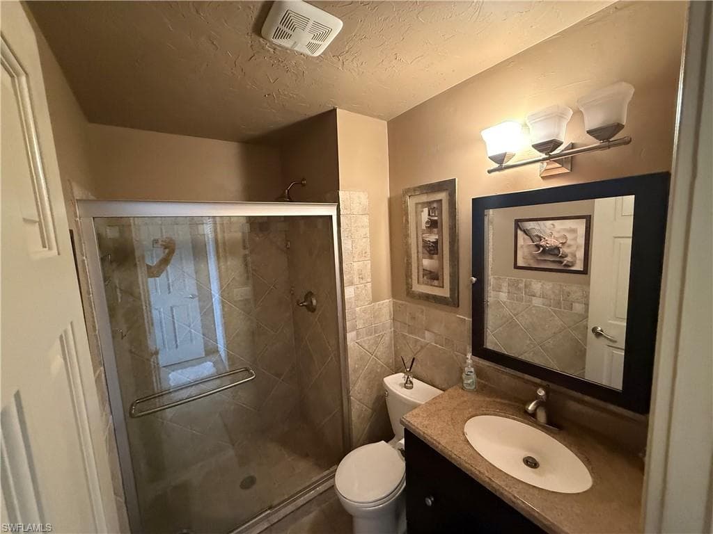 Bathroom featuring a glass-enclosed shower, tiled shower surround, vanity with an integrated sink, framed mirror, and a three-light fixture