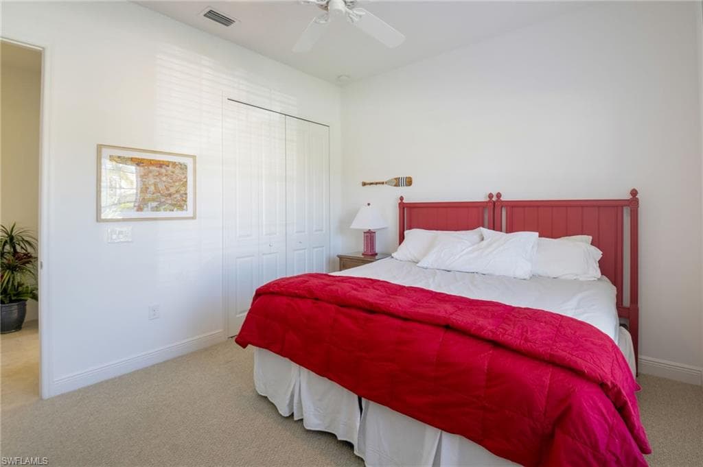 Neutral-toned carpeting spans this room featuring white walls and a white ceiling fan