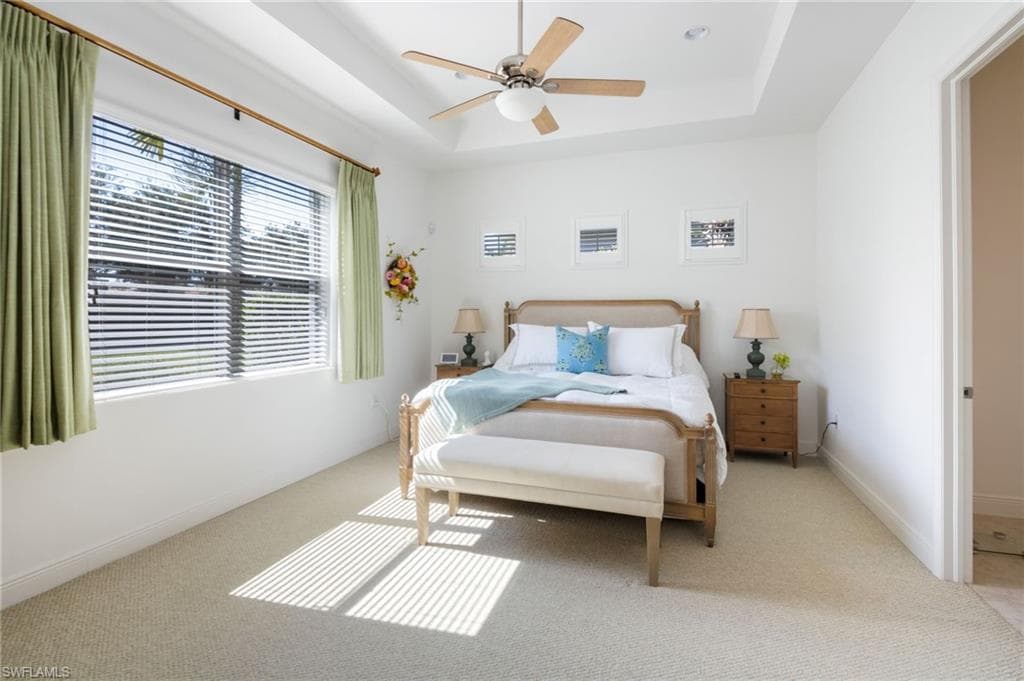 Spacious room featuring a tray ceiling with a ceiling fan, a large window with blinds, and light-colored carpet flooring