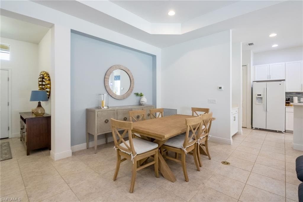 Dining area featuring neutral tile flooring, a tray ceiling, and an accent wall