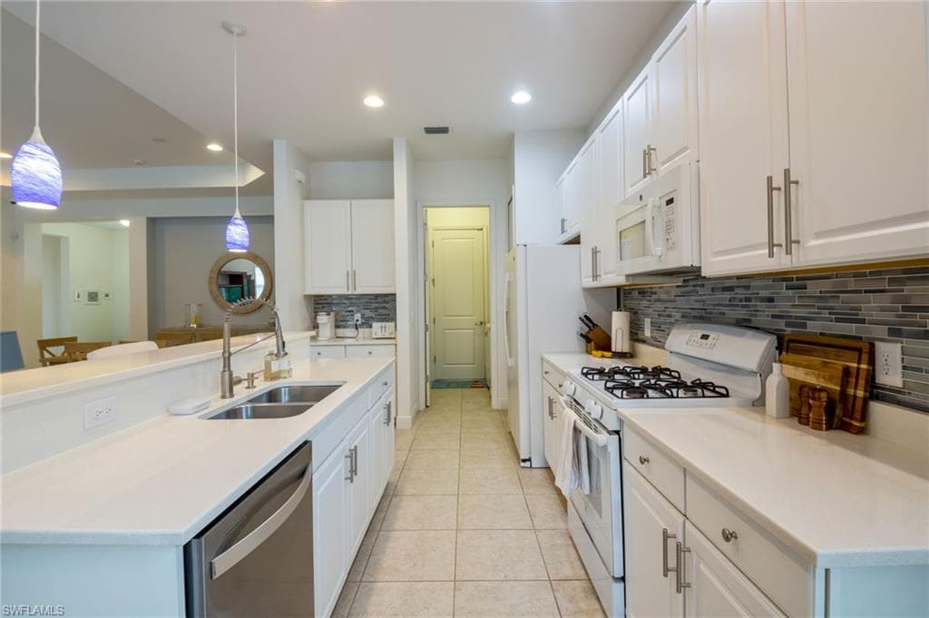 Modern kitchen featuring white cabinetry, light countertops, a tile backsplash, stainless steel sink, and pendant lighting