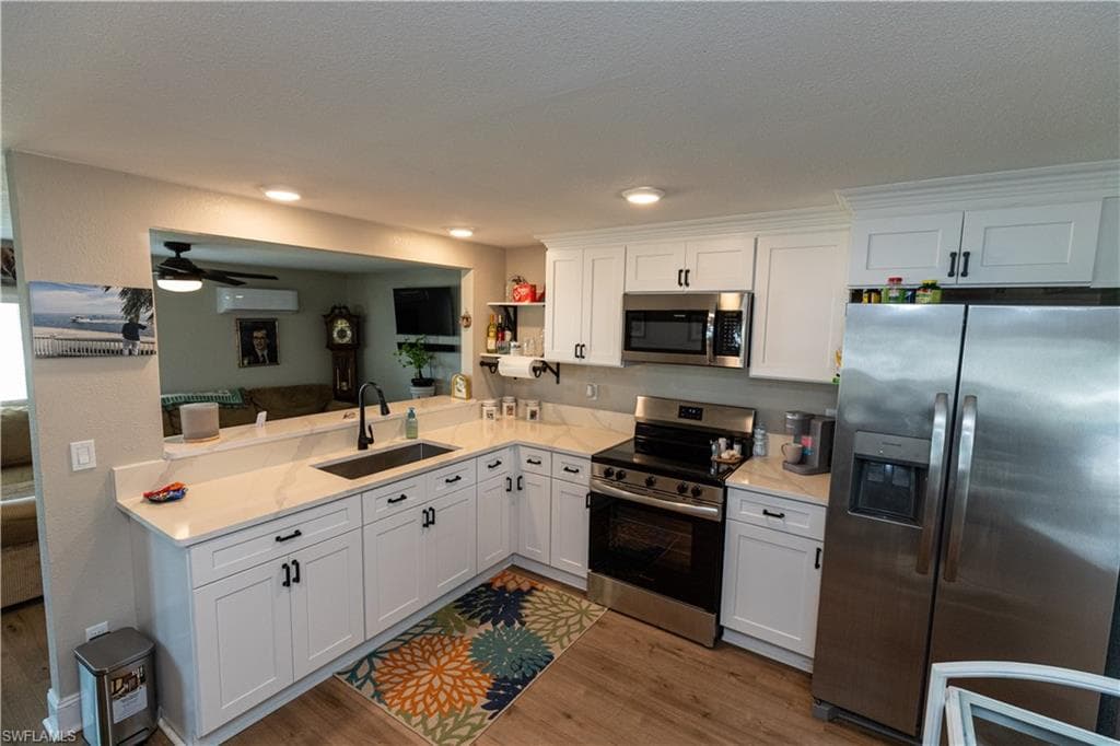 Kitchen featuring white shaker-style cabinetry, stainless steel appliances, a built-in microwave, wood-finish flooring, and light-toned countertops