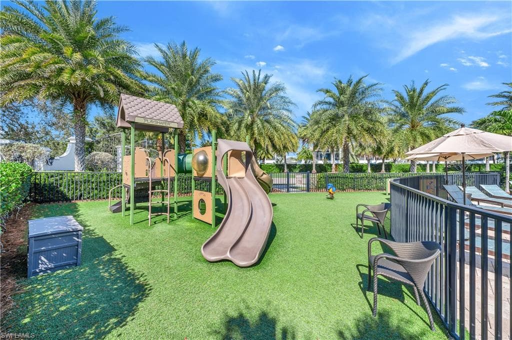 Recreational area featuring artificial turf, a multi-level play structure with slides, and mature palm trees