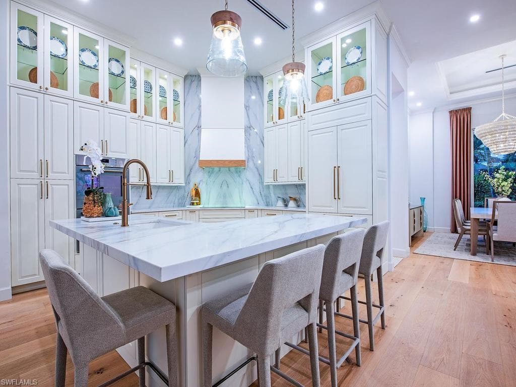 Gourmet kitchen featuring a substantial island with stone countertop, extensive custom cabinetry with glass-front uppers, a built-in oven, and wood-finish flooring