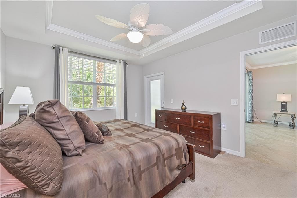 Spacious primary suite featuring a tray ceiling, large window with peaceful preserve views, plush carpeting, and a relaxing retreat-like atmosphere.