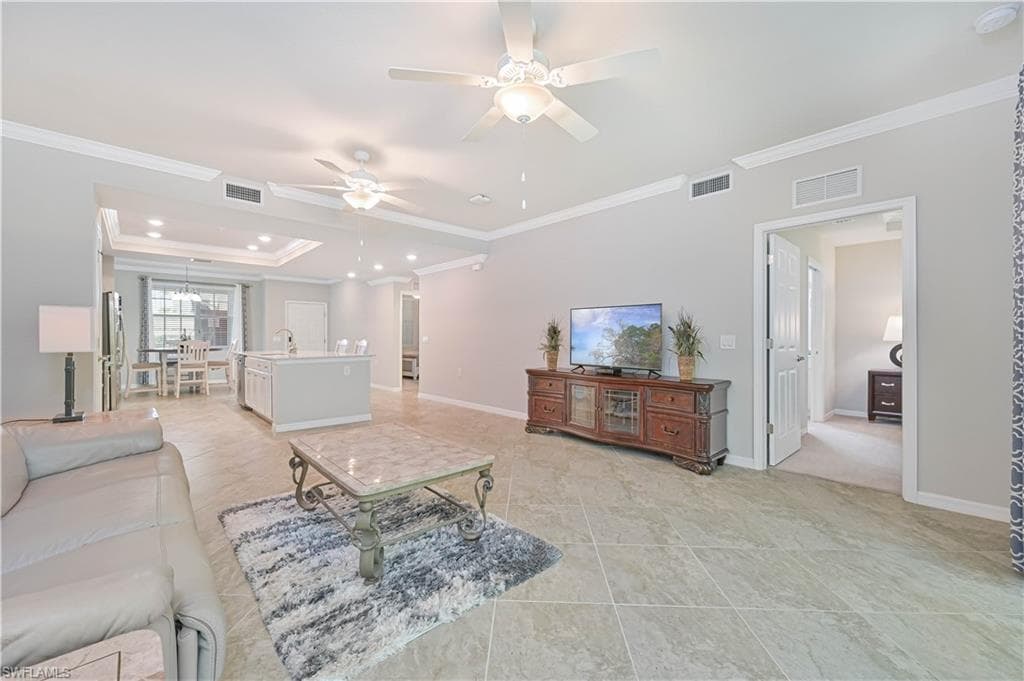 Spacious open-concept great room featuring volume ceilings, crown molding, large-format tile flooring, and seamless flow to the kitchen and dining areas.