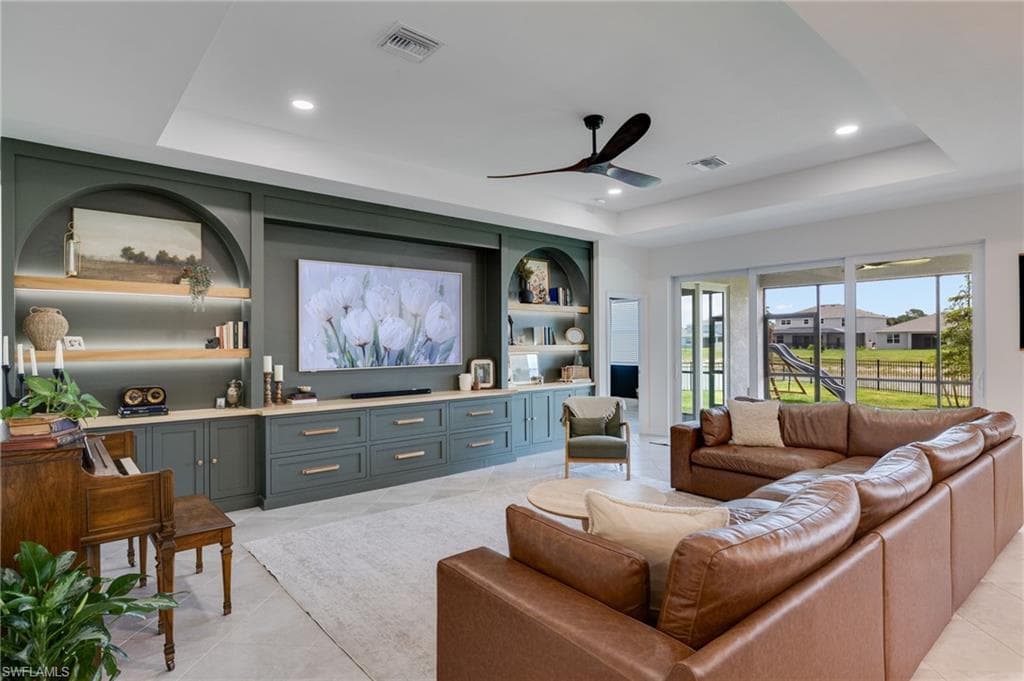 Spacious living area featuring a custom built-in entertainment unit with shelving and integrated lighting, tray ceiling, recessed lighting, and a ceiling fan
