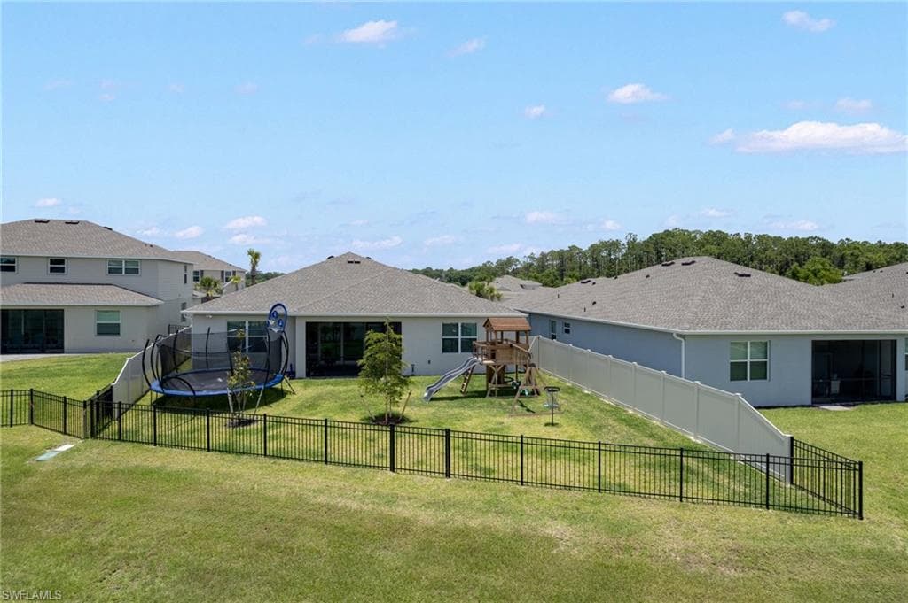 Expansive backyard featuring a black metal fence, mature trees, and a screened lanai